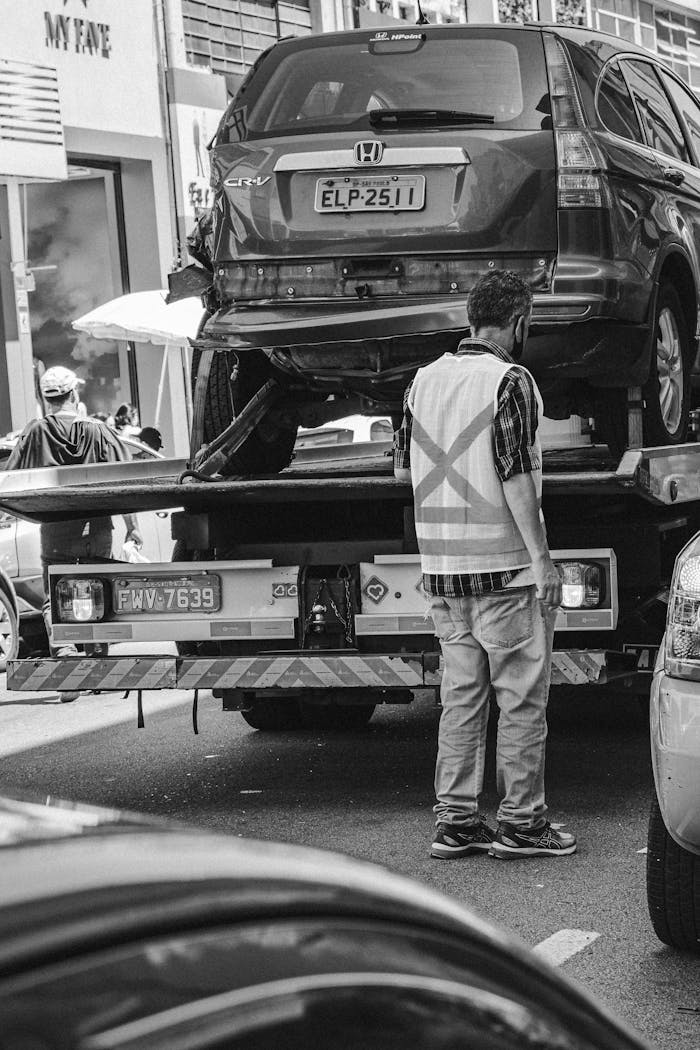 home-hero Grayscale image of a tow truck loading a vehicle on a busy street in São Paulo.