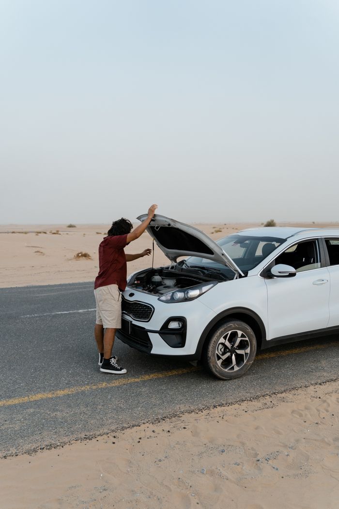 services-05 A man inspecting the engine of a car by the roadside in a desert setting.